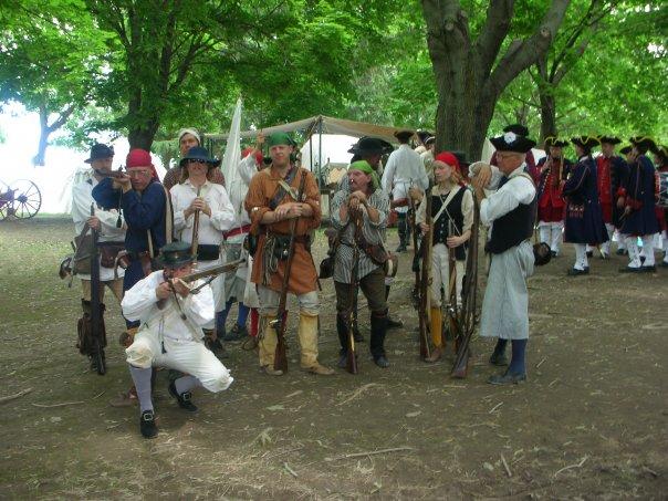 Militia in hunting shirts under trees, one kneeling with a long rifle