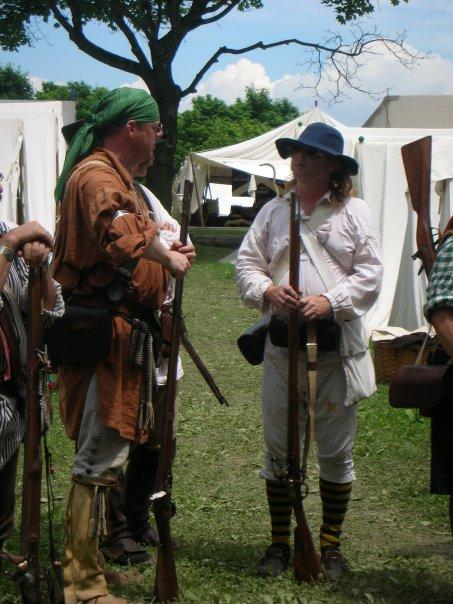 Two re-enactors in camp with muskets, canvas tents behind them