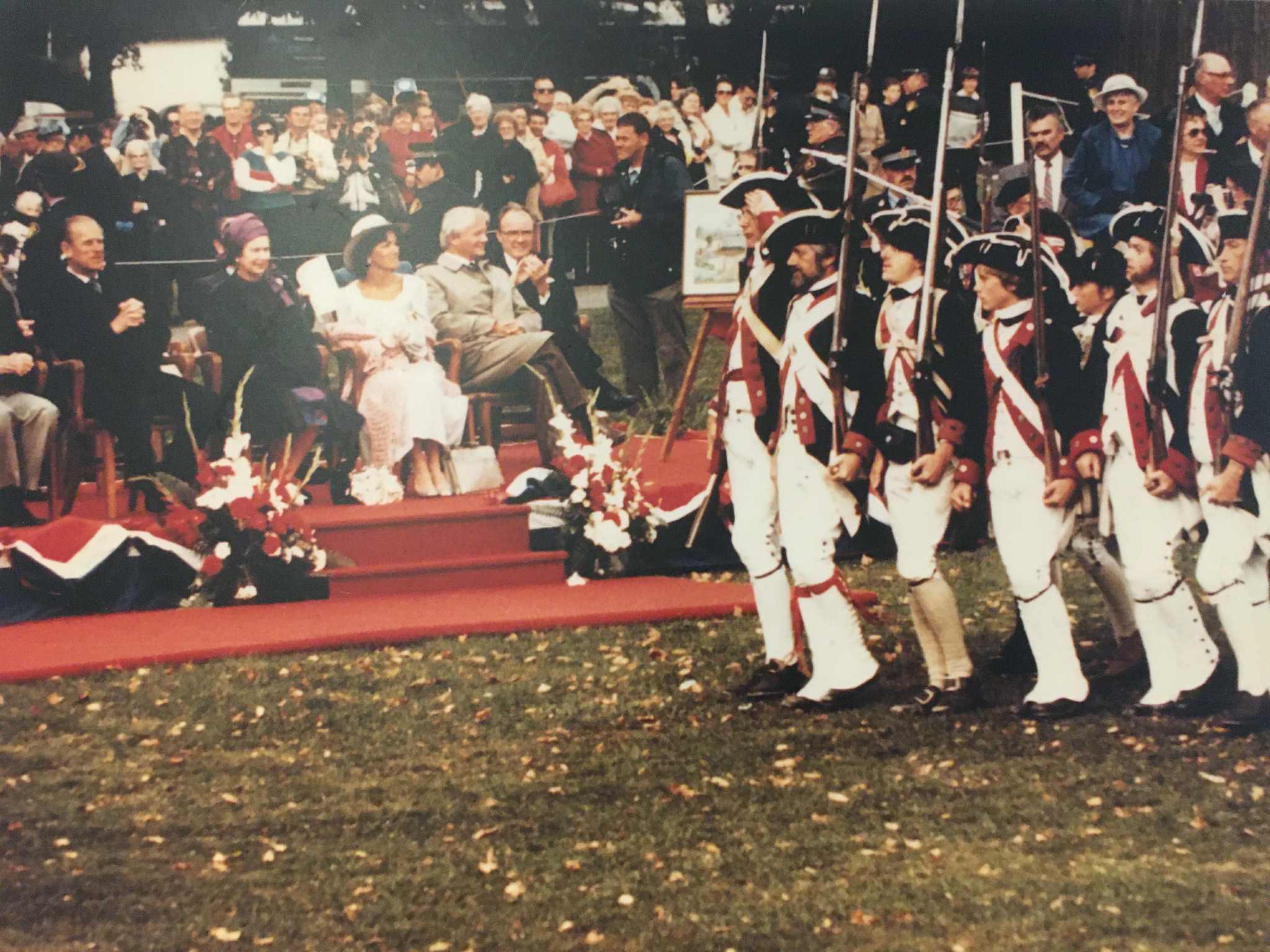Re-enactors in Continental-style uniforms saluting dignitaries on a reviewing stand
